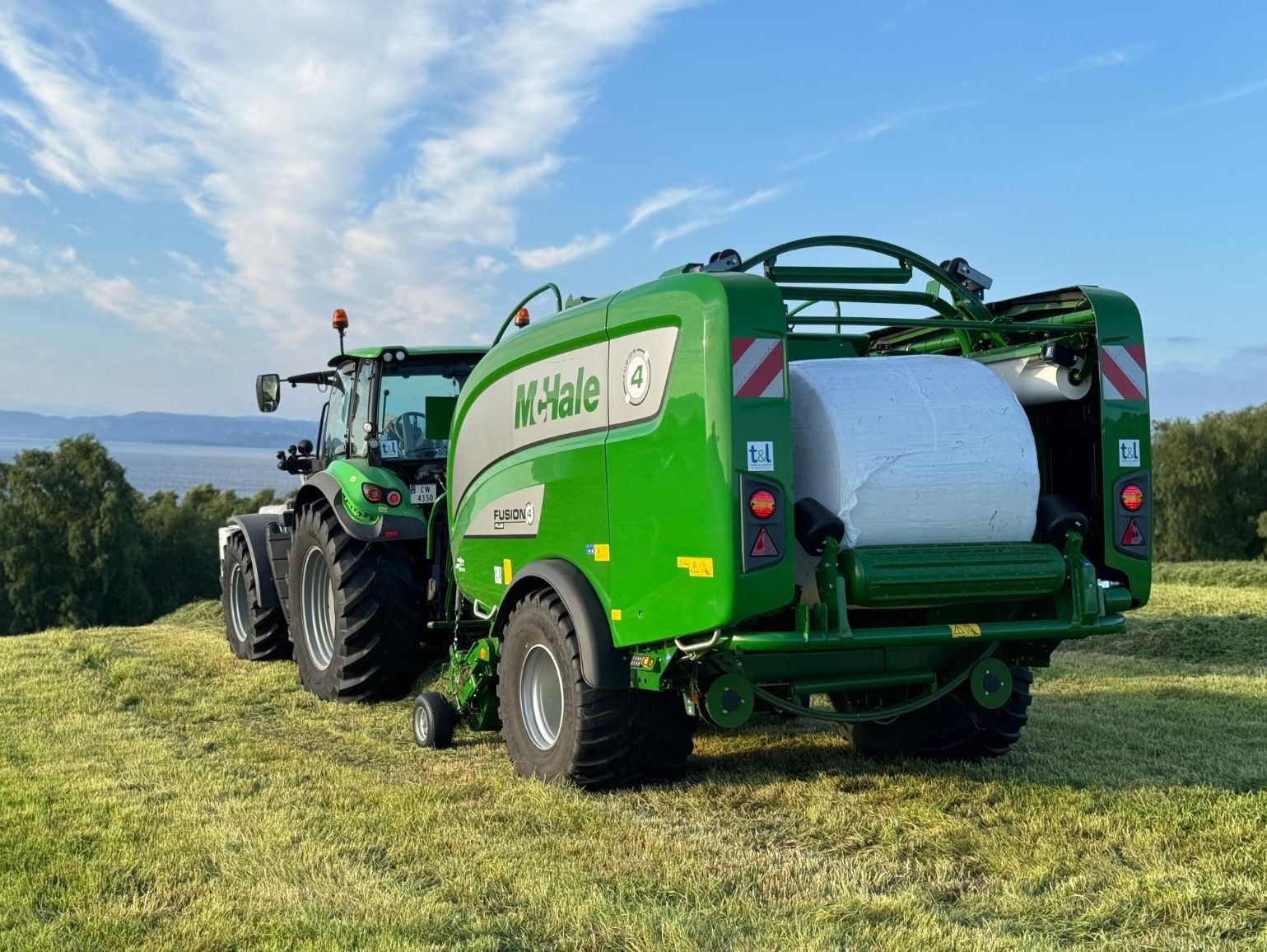 Grønn McHale rundballepresser bak traktor på jorde